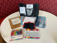 Sketchbook, thick 8x11 paper, ink pencils, brush markers, glitter pens, coloring book, pencils, pens, erasers, and a pencil sharpener on a white round table