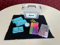 Black felt sheet, 2 large bead trays, 2 small bead trays, scissors, stretch string, a tray of pony beads, and a tray of special beads and clasps.