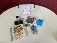 A puzzle book, The Genius Square, a maze cube, Kanoodle, Rotate & Slide Puzzle, Scramboozle, and a Rubik's cube on a white round table