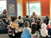 Librarian reading to a group of children with parents sitting in the back of the group