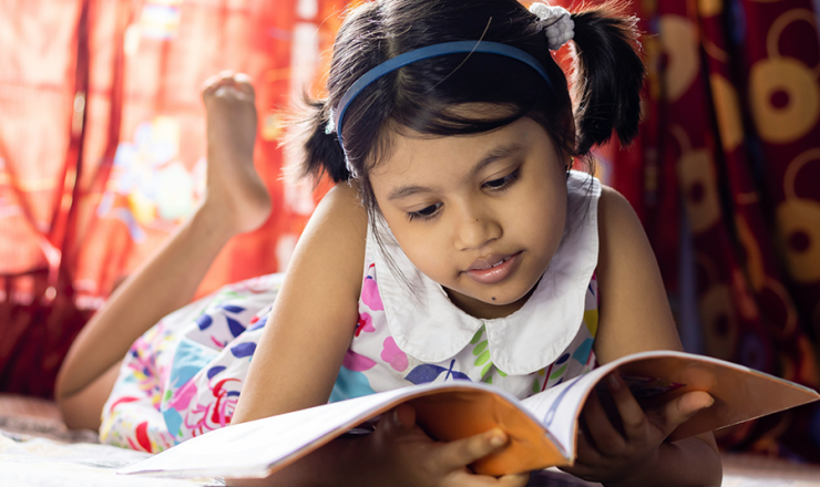 Young girl with headphones on reading a book
