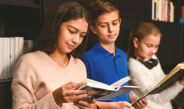 Two teen girls and a teen boy standing with open books in their hands